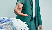 A man in a green suit accepting a wad of £20 bills
