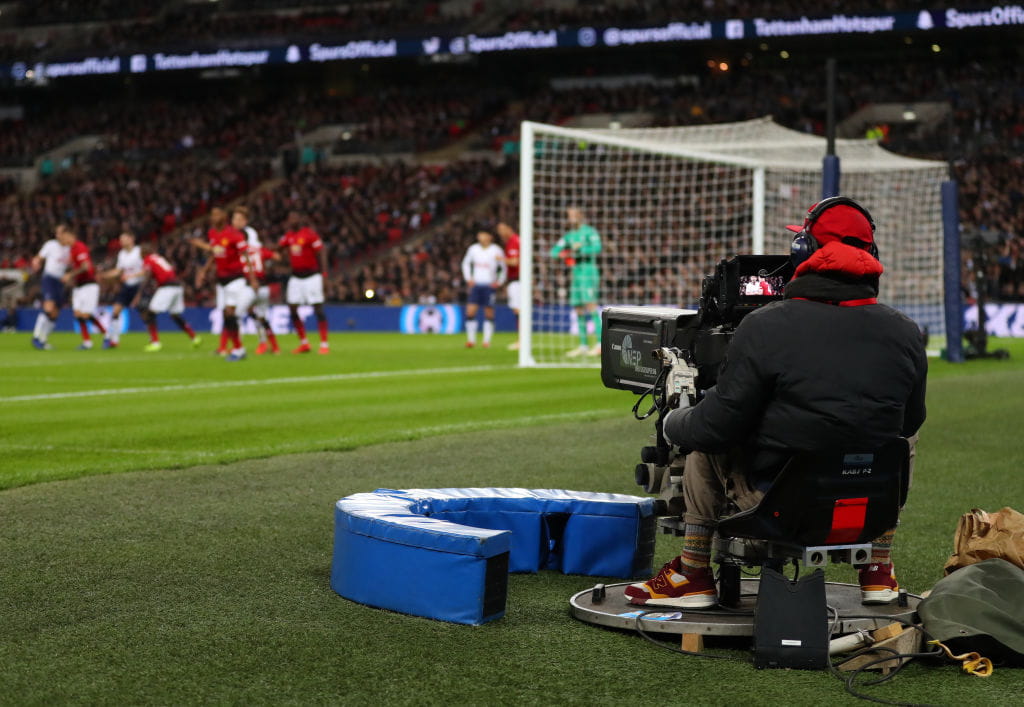 A cameraman follows the action pitchside at a Premier League match.