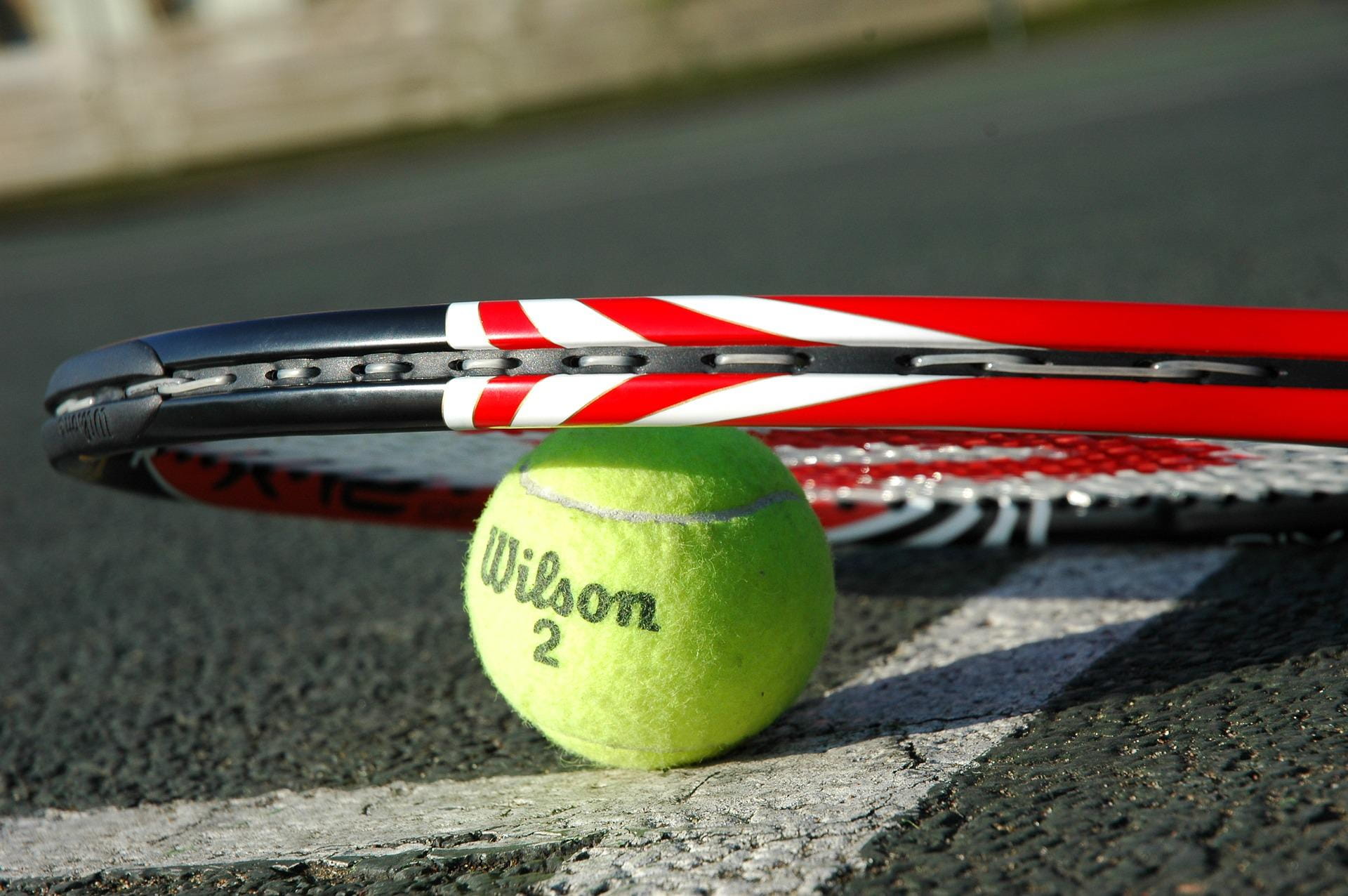 A picture of a tennis racquet placed onto a Wilson branded tennis ball.