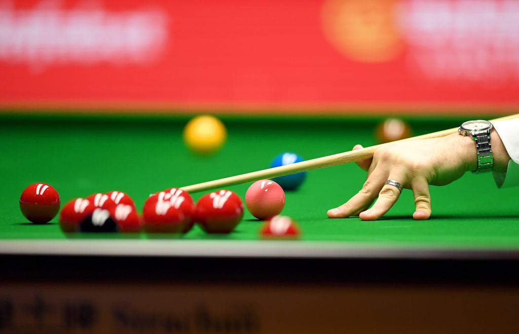 A close-up of an arched hand as a difficult snooker shot is played.