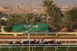 Horses galloping past a Saudi Cup sign at Riyadh King Abdulaziz Racecourse.