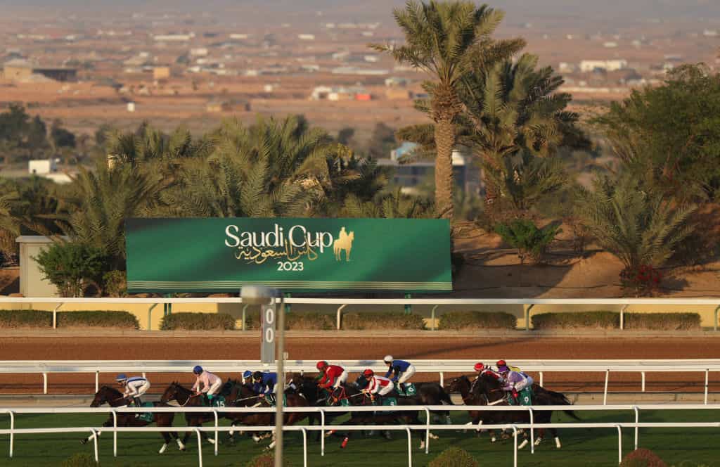 Horses galloping past a Saudi Cup sign at Riyadh King Abdulaziz Racecourse.