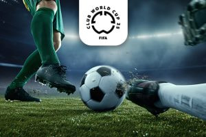 A dramatic close-up image of a football match moment, showing a player in green kit and black boots poised to kick a black-and-white football while an opposing goalkeeper's gloved hand reaches for the ball on the grass. The scene is set in a floodlit stadium, highlighting the intensity of the game. Above the action is the logo for the FIFA Club World Cup 25, signalling a prestigious tournament.