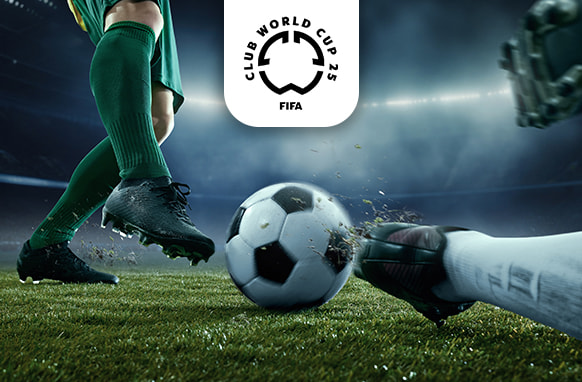 A dramatic close-up image of a football match moment, showing a player in green kit and black boots poised to kick a black-and-white football while an opposing goalkeeper's gloved hand reaches for the ball on the grass. The scene is set in a floodlit stadium, highlighting the intensity of the game. Above the action is the logo for the FIFA Club World Cup 25, signalling a prestigious tournament.