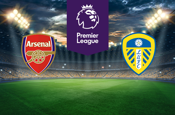The image shows the logos of two Premier League football clubs, Arsenal and Leeds United, displayed on a football pitch background. The Arsenal logo is on the left side, featuring a red shield with a cannon and the text "Arsenal." The Leeds United logo is on the right side, featuring a shield with yellow and blue stripes, a white rose at the top, and the text "LUFC." In the centre, there is the Premier League logo, consisting of a lion's head above the text "Premier League." The background depicts a lit football stadium with a dramatic, cloudy sky above, creating an intense and competitive atmosphere.
