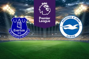 The image shows the logos of two Premier League football clubs, Everton and Brighton & Hove Albion, displayed on a football pitch background. The Everton logo is on the left side, featuring a blue shield with a depiction of Prince Rupert's Tower, laurel wreaths on either side, and the club's motto "Nil Satis Nisi Optimum" along with the text "Everton 1878." The Brighton & Hove Albion logo is on the right side, featuring a blue circle with a white seagull flying across it and the text "Brighton & Hove Albion." In the centre, there is the Premier League logo, consisting of a lion's head above the text "Premier League." The background depicts a lit football stadium with a dramatic, cloudy sky above, creating an intense and competitive atmosphere.