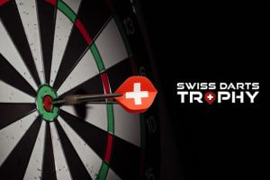 The image features a close-up of a dartboard with a dart successfully hitting the bullseye. The dart's flight is adorned with a red design featuring a white cross, reminiscent of the Swiss flag. To the right of the dartboard, the text "Swiss Darts Trophy" is displayed, with the word "Trophy" stylised to include a small red diamond with a white cross in place of the letter "O" in "Trophy," echoing the Swiss national flag. The overall visual composition emphasises precision and national pride, creating a focused and compelling atmosphere for the Swiss Darts Trophy event.