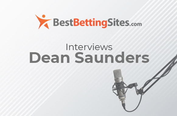 A light grey background with diagonal lines. At the top, the logo for BestBettingSites.com features an orange abstract figure and text. Below that, the text reads "Interviews Dean Saunders." On the right side, a microphone on a stand is shown.