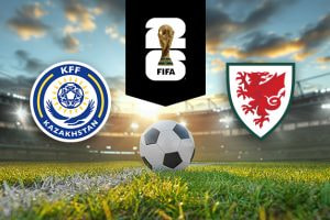 The image shows the logos of two national football associations, the Kazakhstan Football Federation and the Football Association of Wales, displayed on a football pitch with a football in the centre. The Kazakhstan logo is on the left, featuring a blue and yellow circular design with the text "KFF Kazakhstan." The Wales logo is on the right, featuring a red dragon on a shield. In the centre above the football is the FIFA logo, which includes the FIFA World Cup Trophy and "FIFA" below it on a black background. The setting is a stadium with dramatic sky lighting, giving it a dynamic and intense atmosphere.