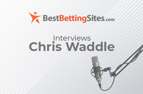 The image features a graphic for an interview segment. At the top, there is a logo and text for "BestBettingSites.com," with "BestBettingSites" in bold and the ".com" in a smaller font. Below the logo, the text reads, "Interviews Chris Waddle" in a clear, bold font. To the right of the text, there is an image of a professional microphone attached to an adjustable arm, suggesting a setup for recording or broadcasting. The background has a light gradient with subtle diagonal lines, creating a clean and professional look.