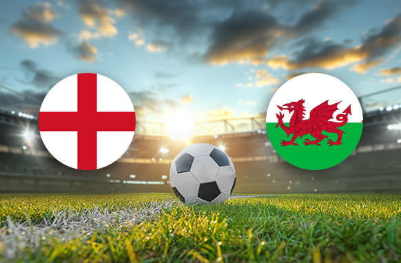 The image features two national football team logos on a football pitch. On the left, there is the flag of England, featuring a red cross of Saint George on a white background. On the right, there is the flag of Wales, which displays a red dragon passant on a green and white field. In the centre of the image, there is a football placed on the grass. The background depicts a stadium with a scenic sky showing a blend of clouds and sunlight, casting a warm, ambient glow over the scene. The overall composition creates an atmosphere of anticipation and excitement, highlighting the impending football match between the two nations.