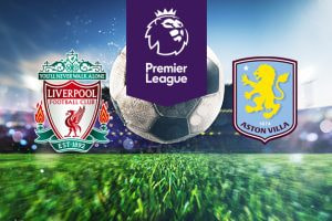The image features logos of two Premier League football teams. On the left is Liverpool's logo with "You'll Never Walk Alone" above it. On the right is Aston Villa's logo with a lion and the year 1874. Above the logos is the Premier League logo with a lion's head and "Premier League" on a purple background. In the background, a stadium is visible with a large football in the centre, creating an atmosphere of anticipation.