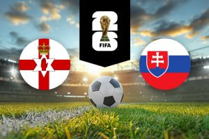 The image features two national football team logos on a football pitch. On the left, there is the flag of Northern Ireland, featuring a red cross with a white hand and a crown positioned in the centre on a white background. On the right, there is the flag of Slovakia, consisting of white, blue, and red horizontal stripes with a red shield containing a white cross and three blue hills on the left side. In the centre of the image, there is a football placed on the grass. Above the football, there is the FIFA World Cup logo with the FIFA trophy enclosed in a black vertical stripe, symbolising the tournament. The background depicts a stadium with dramatic lighting and a picturesque sky with clouds, creating an atmosphere of anticipation and excitement.