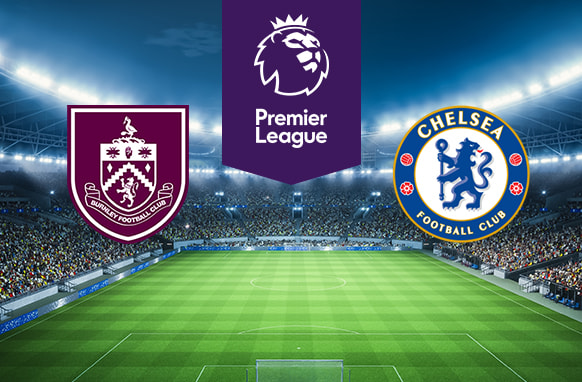 The image features logos representing two football clubs participating in a Premier League match. On the left is the logo of Burnley Football Club, which includes a shield with various symbols and a claret and blue colour scheme. On the right is the logo of Chelsea Football Club, featuring a blue lion holding a staff with red roses and footballs around the edge. Above the logos is the Premier League logo, featuring a lion's head with a crown and the text "Premier League" beneath it. The background shows a brightly lit football stadium filled with spectators, enhancing the feeling of competition and anticipation for the upcoming match. The pitch is well-maintained and ready for play, completing the scene.