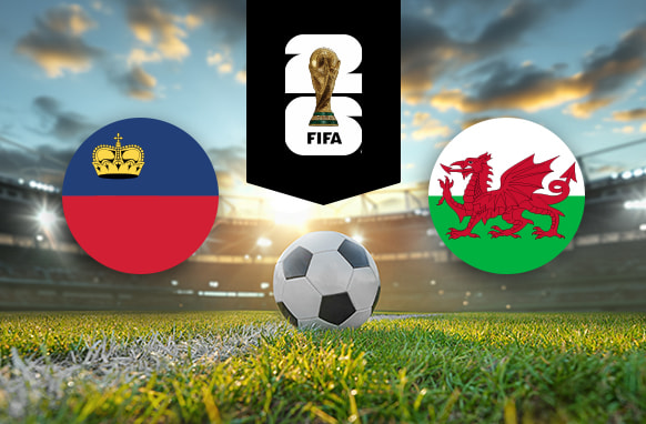 The image features flags representing two football teams participating in an international event. On the left is the flag of Liechtenstein, which consists of two horizontal stripes in blue and red with a golden crown on the blue stripe. On the right is the flag of Wales, which features a red dragon passant on a green and white field. Above the flags is the FIFA 2026 World Cup logo, depicting the World Cup trophy with the number "26." The background shows a brightly lit stadium at sunset with a football placed on the pitch in the centre, creating an atmosphere of competition and anticipation for the upcoming match.