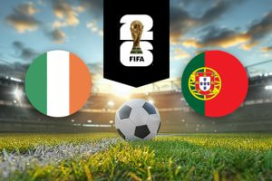 The image features logos and flags representing two football teams participating in an international event. On the left is the flag of Ireland, which consists of three vertical stripes in green, white, and orange. On the right is the flag of Portugal, featuring a red and green background with a coat of arms in the middle. Above the flags is the FIFA 2022 World Cup logo, depicting the World Cup trophy. The background depicts a brightly lit stadium at sunset, with a football placed on the pitch in the centre, creating an atmosphere of competition and anticipation for the upcoming match.